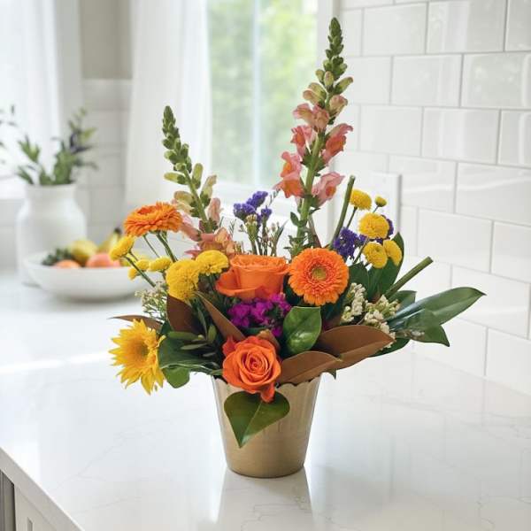 Bright mixed flower arrangement in a gold vase on a kitchen counter