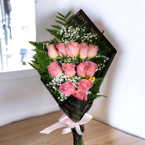 Bouquet of pink roses with baby's breath wrapped in black paper and tied with a pink ribbon