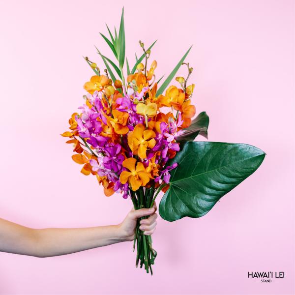 Handheld bouquet of orange and purple orchids with large tropical leaves