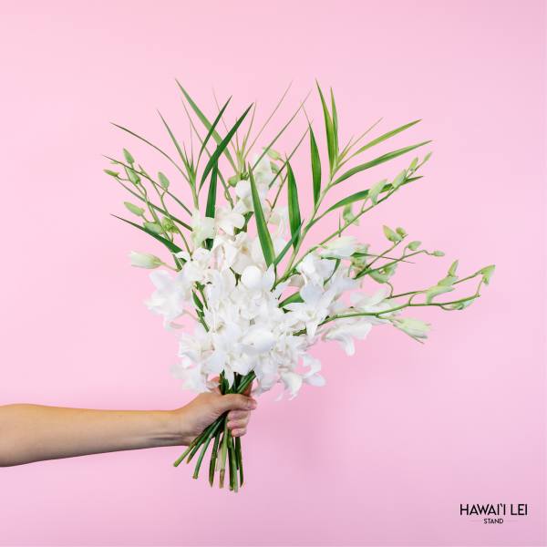 Handheld bouquet of white orchids with long green leaves against a pink background
