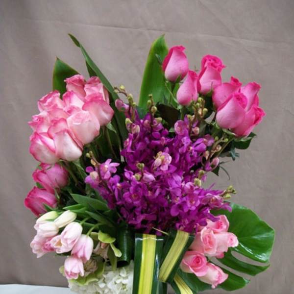 Pink roses and purple orchids arranged in a glass vase