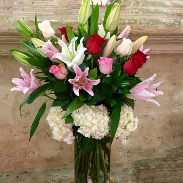 Tall bouquet of pink and red roses with lilies in a glass vase