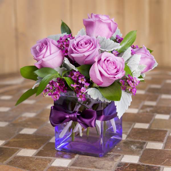 Pink roses arranged in a purple glass vase with a ribbon