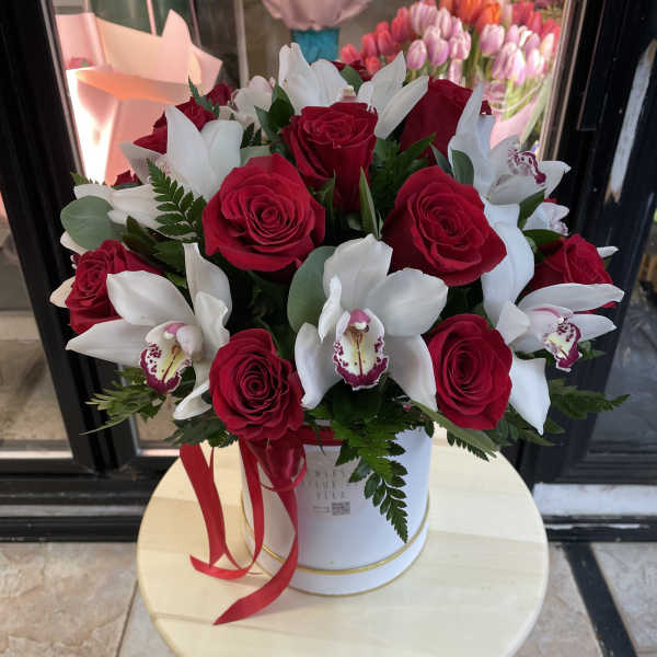 Red roses and white orchids arranged in a white hatbox with a red ribbon
