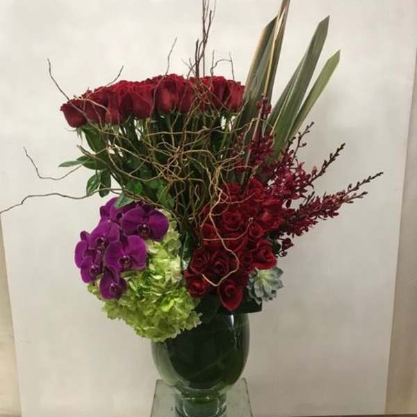 Tall bouquet of red roses, purple orchids, and green hydrangeas in a glass vase