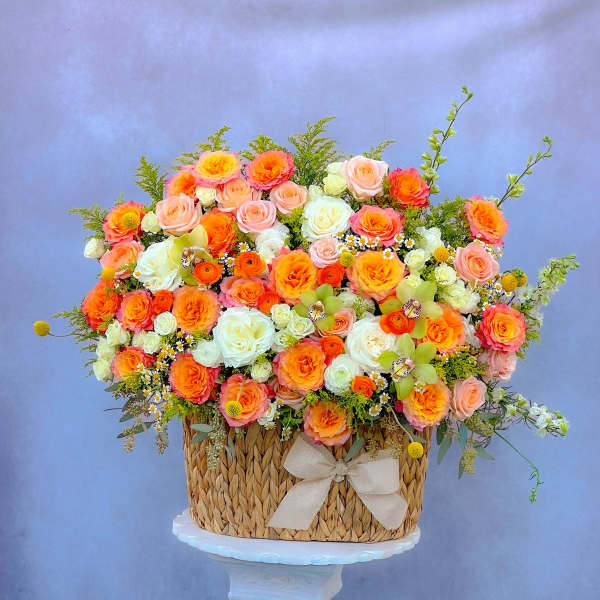 Basket arrangement of orange, pink, and white roses with a ribbon bow