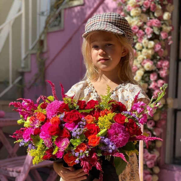 Girl holding a large bouquet of bright mixed flowers in a black container