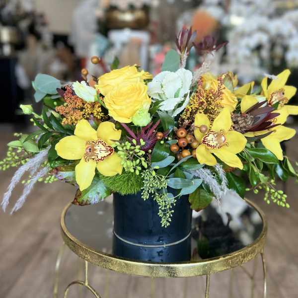 Yellow roses and orchids arranged in a dark vase