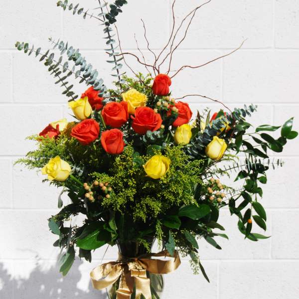 Bouquet of red and yellow roses in a glass vase with a gold ribbon