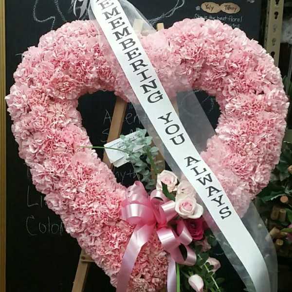 Pink heart-shaped floral wreath with a memorial ribbon on an easel