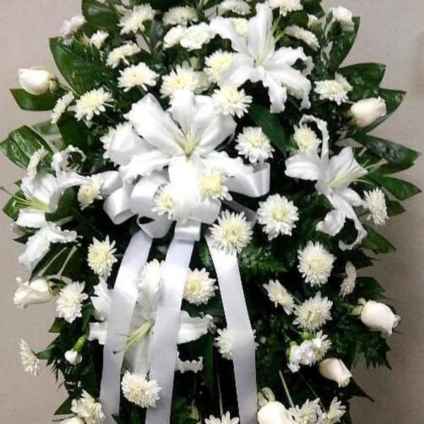 White funeral spray with lilies, mums, and ribbon on an easel