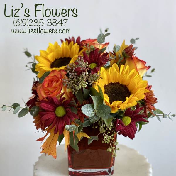 Bouquet of sunflowers, roses, and burgundy daisies in a red glass vase