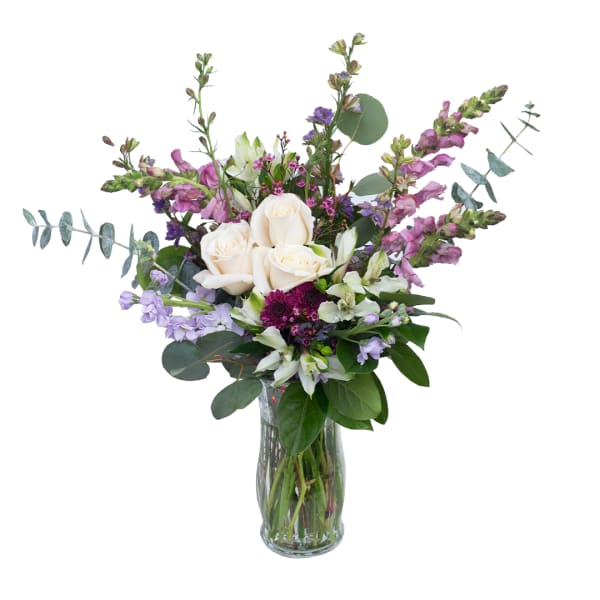 Bouquet of white roses and purple flowers in a clear glass vase