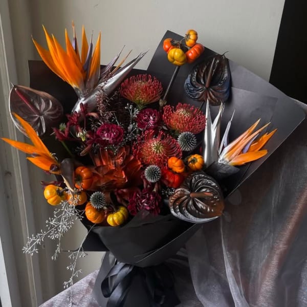 Bouquet with orange bird-of-paradise and dark tropical blooms wrapped in black paper