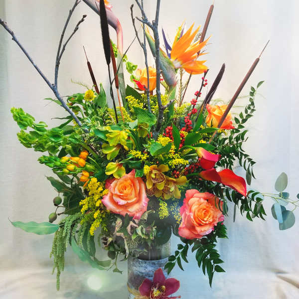 Tall tropical floral arrangement with orange roses and bird of paradise in a vase