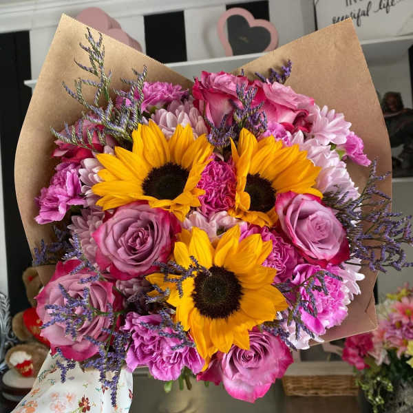 Bouquet of yellow sunflowers, pink roses, and purple flowers wrapped in brown paper
