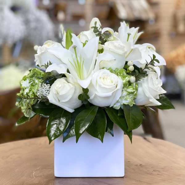 White lilies and roses arranged in a white square vase