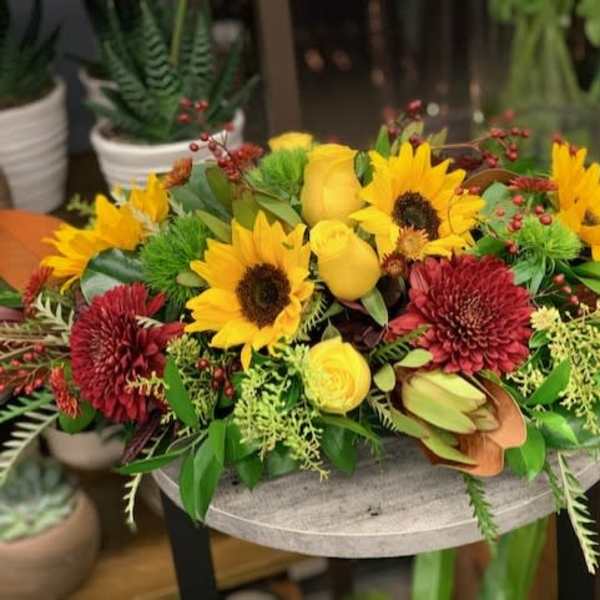 Yellow sunflowers and red blooms arranged in a low centerpiece
