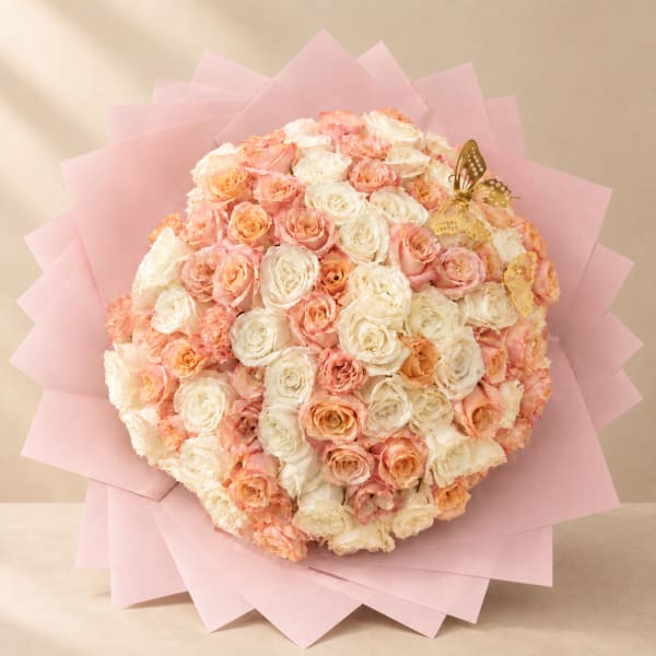 Round bouquet of peach and white roses wrapped in pink paper