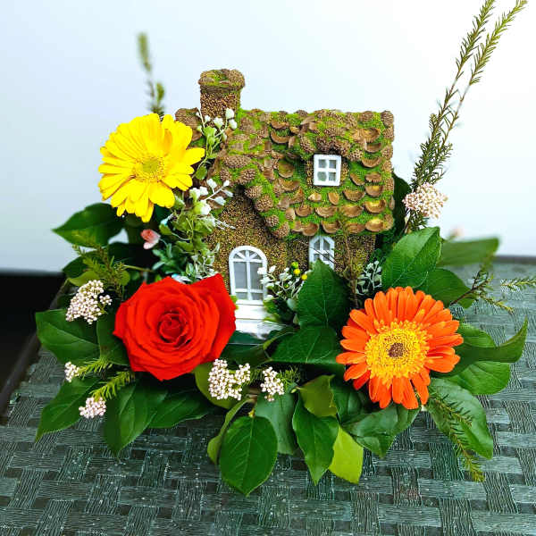 Miniature house surrounded by red, yellow, and orange flowers