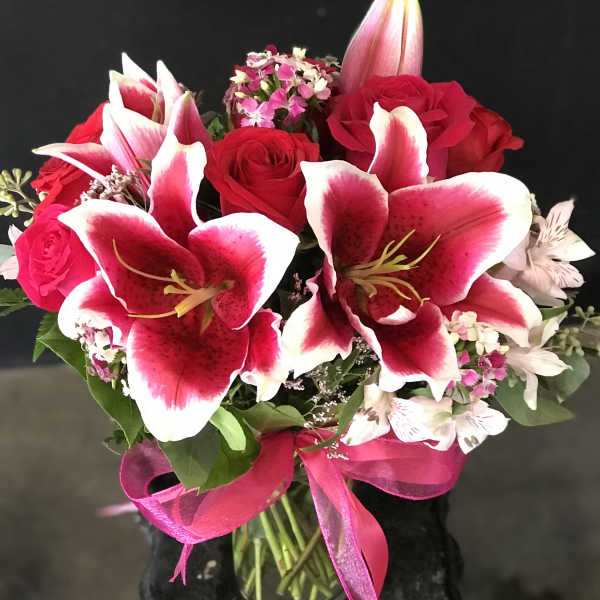 Arrangement of pink lilies and red roses in a clear glass vase with a pink ribbon bow