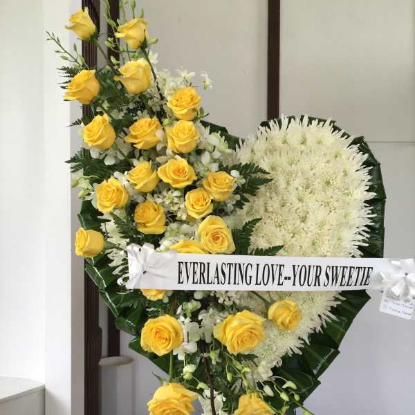 Yellow roses and white flowers arranged on a standing easel with a ribbon banner