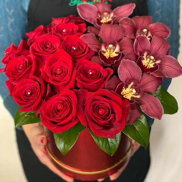 Red roses and burgundy orchids arranged in a round box