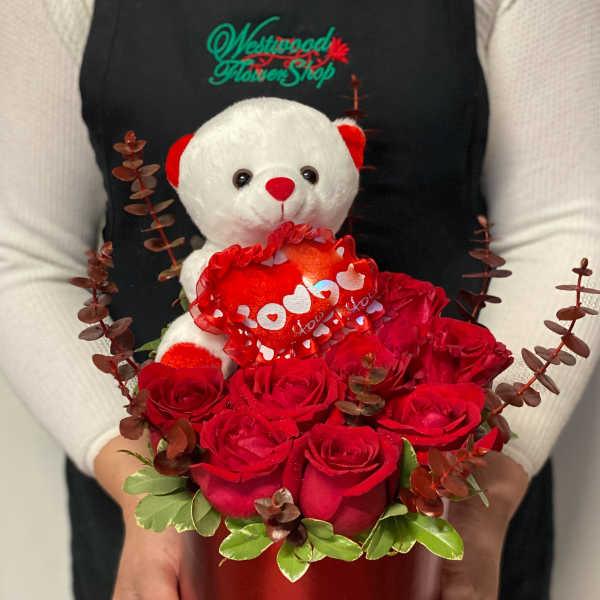 Red roses in a round box with a teddy bear holding a heart