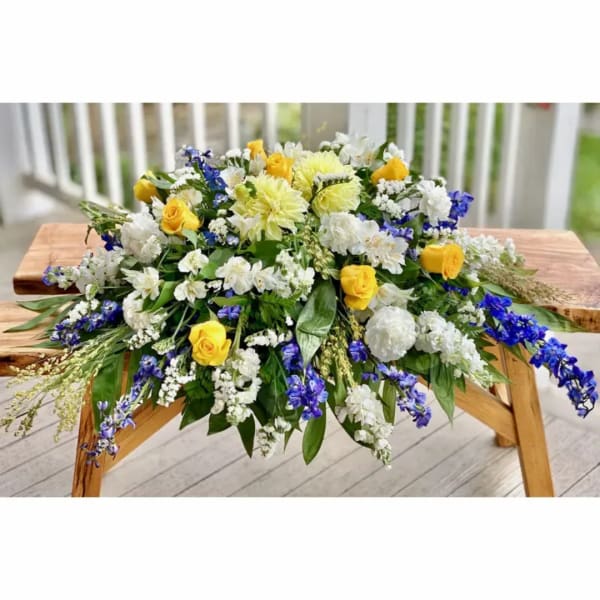 Large floral arrangement with yellow roses, white blooms, and blue flowers on a wooden table