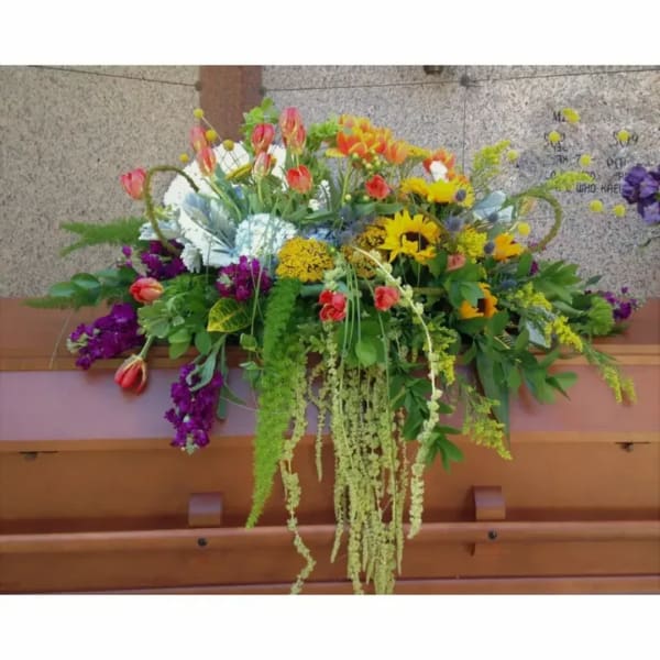 Large colorful floral arrangement with sunflowers and tulips in a wooden casket spray