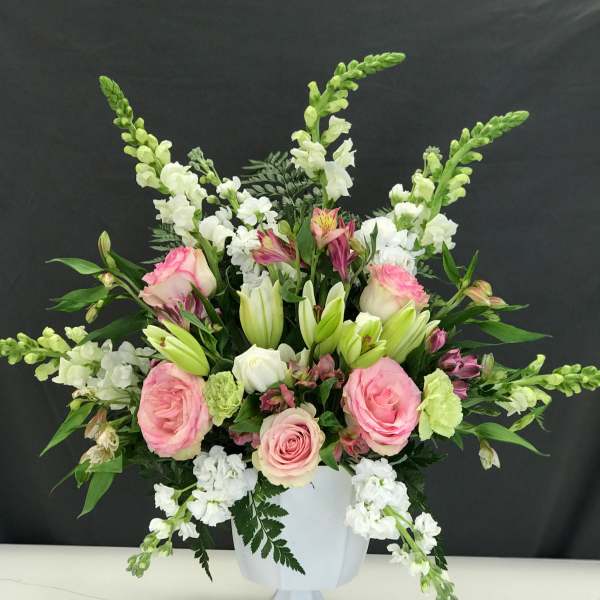 Pink roses and white lilies arranged in a white pedestal vase