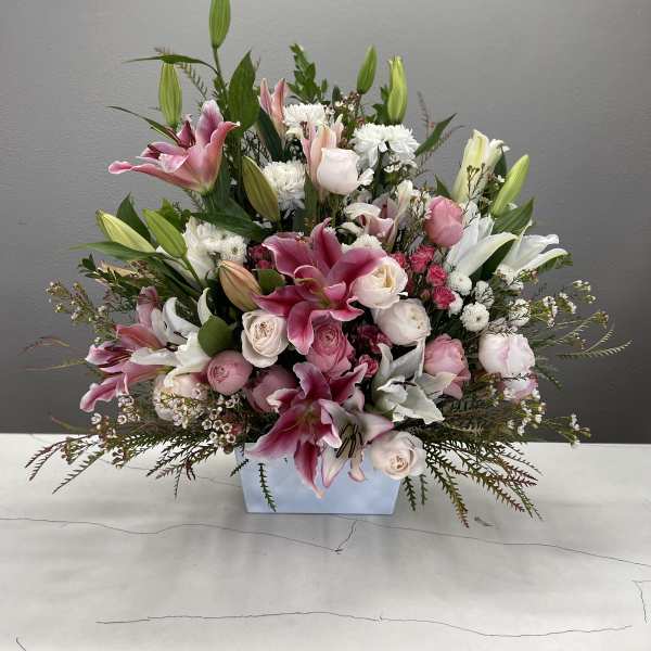Pink and white lilies and roses arranged in a low rectangular vase