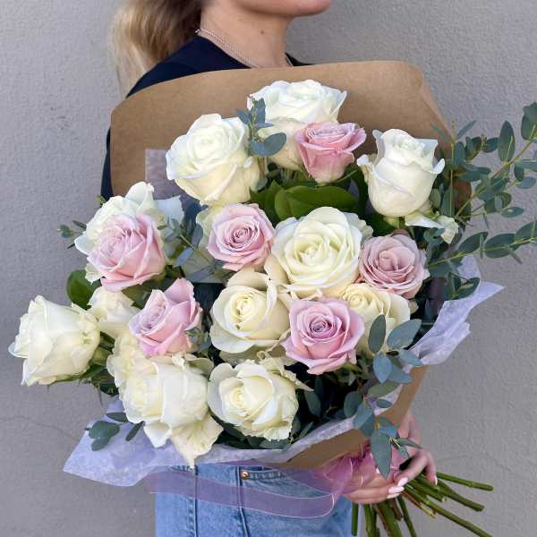 Large hand-tied bouquet of white and pale pink roses wrapped in kraft paper, held by a person.