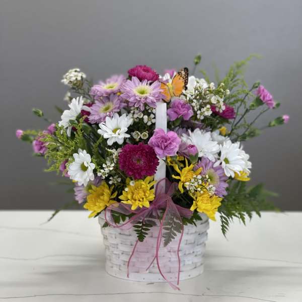 Mixed bouquet in a white basket with pink ribbon and a butterfly pick