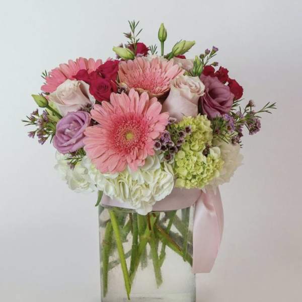 Pink and white mixed bouquet in a clear glass vase with a pink ribbon