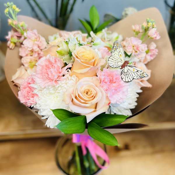 Bouquet of peach roses, pink carnations, and white flowers with a butterfly accent