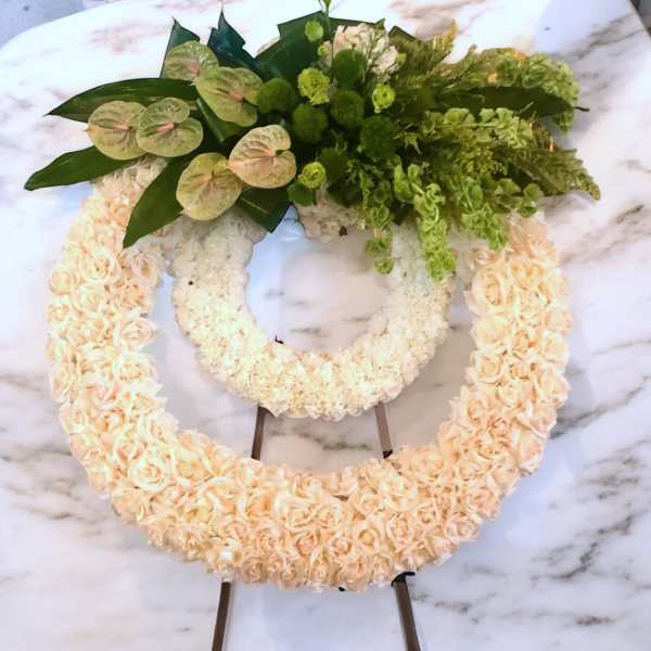 Two floral wreaths with peach roses and green tropical foliage