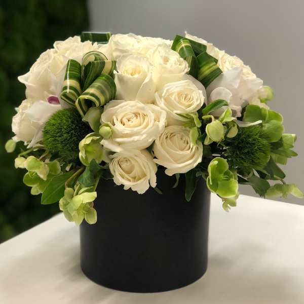 Low round arrangement of white roses and green accents in a black cylinder vase