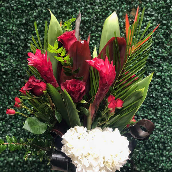 Tall tropical arrangement with red roses and pink blooms above white hydrangeas in a clear glass vase
