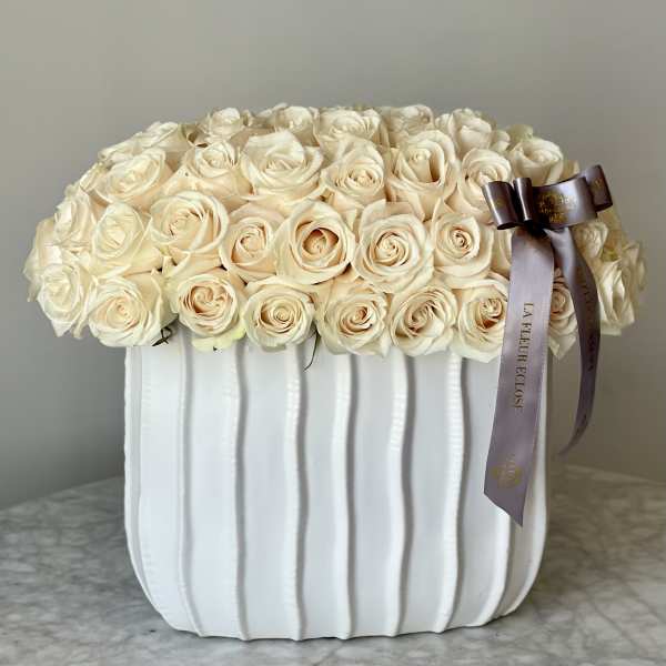 Cream rose arrangement in a white ribbed vase with a ribbon bow