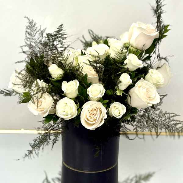 Arrangement of white roses with airy greenery in a tall black cylinder vase