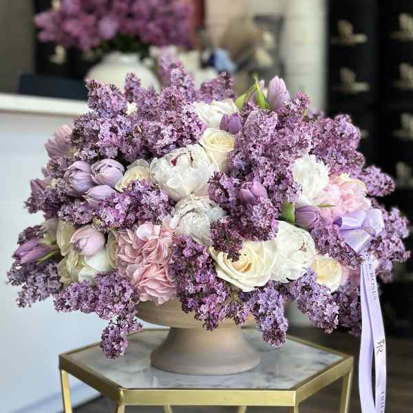 Lavender and white floral arrangement in a beige pedestal vase