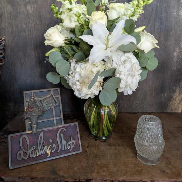 White floral arrangement in a glass vase with roses, lilies, and hydrangeas