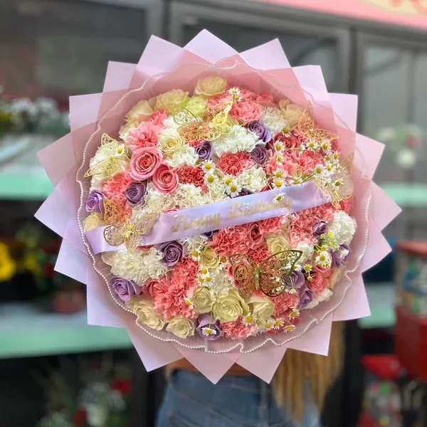 Large pastel bouquet of roses, carnations, and small daisies wrapped in pink paper