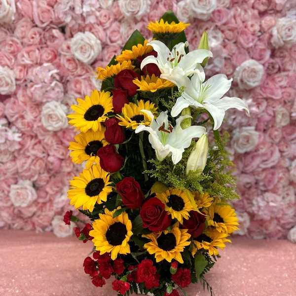 Bouquet of red roses, sunflowers, and white lilies against a pink rose wall