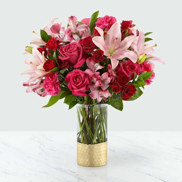 Pink and red mixed bouquet in a clear glass vase with a gold base