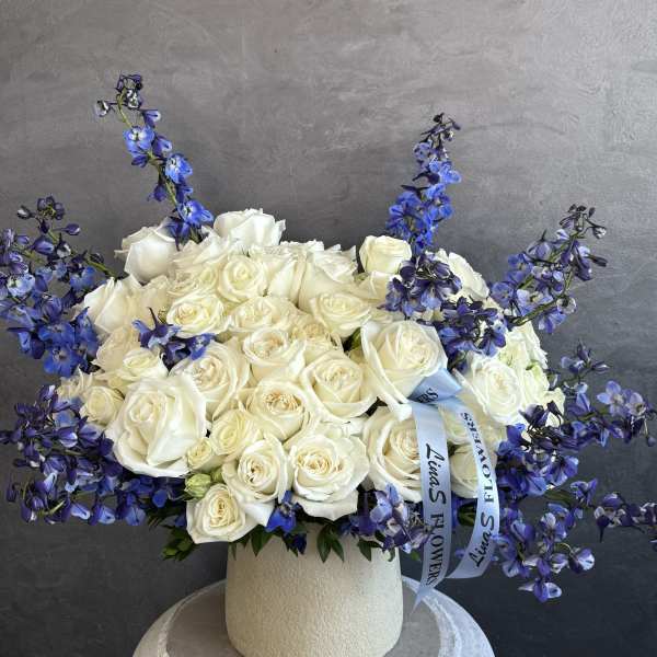 White rose arrangement with blue delphinium in a cream vase