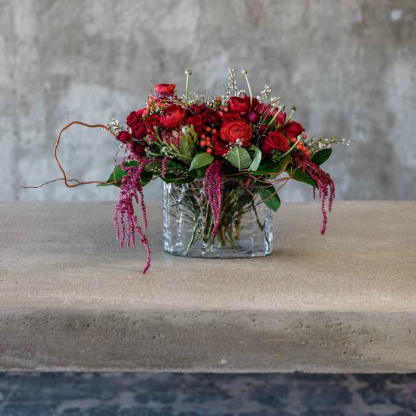 Red rose arrangement in a clear glass vase with trailing pink accents