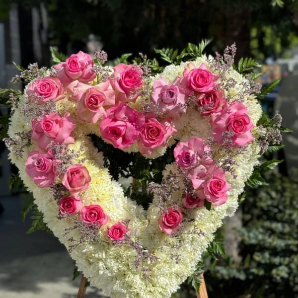 Heart-shaped floral arrangement with pink roses and white flowers on an easel