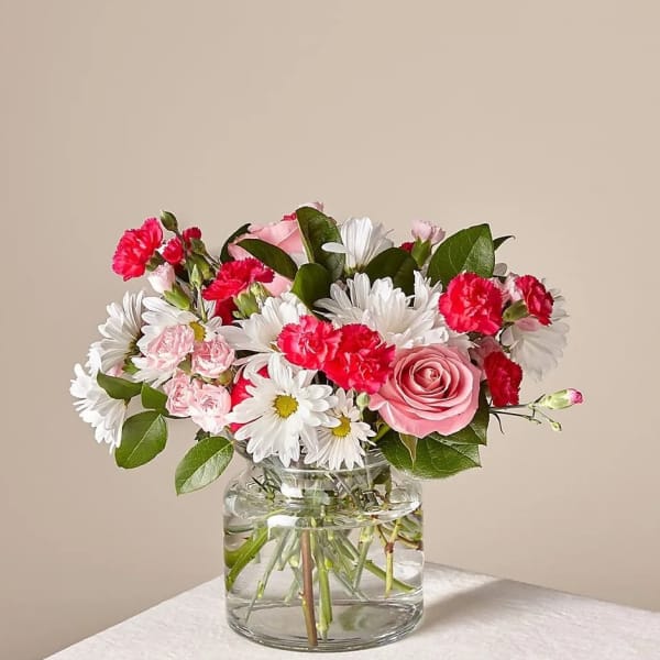 Pink roses, white daisies, and red carnations in a clear glass vase